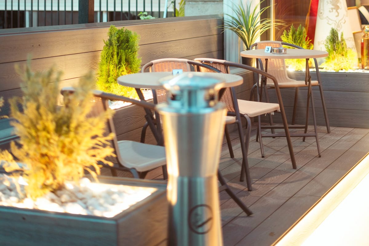 Terrasse eines Restaurants in der Dämmerung mit Bistrotischen, Stühlen und einem Heizstrahler