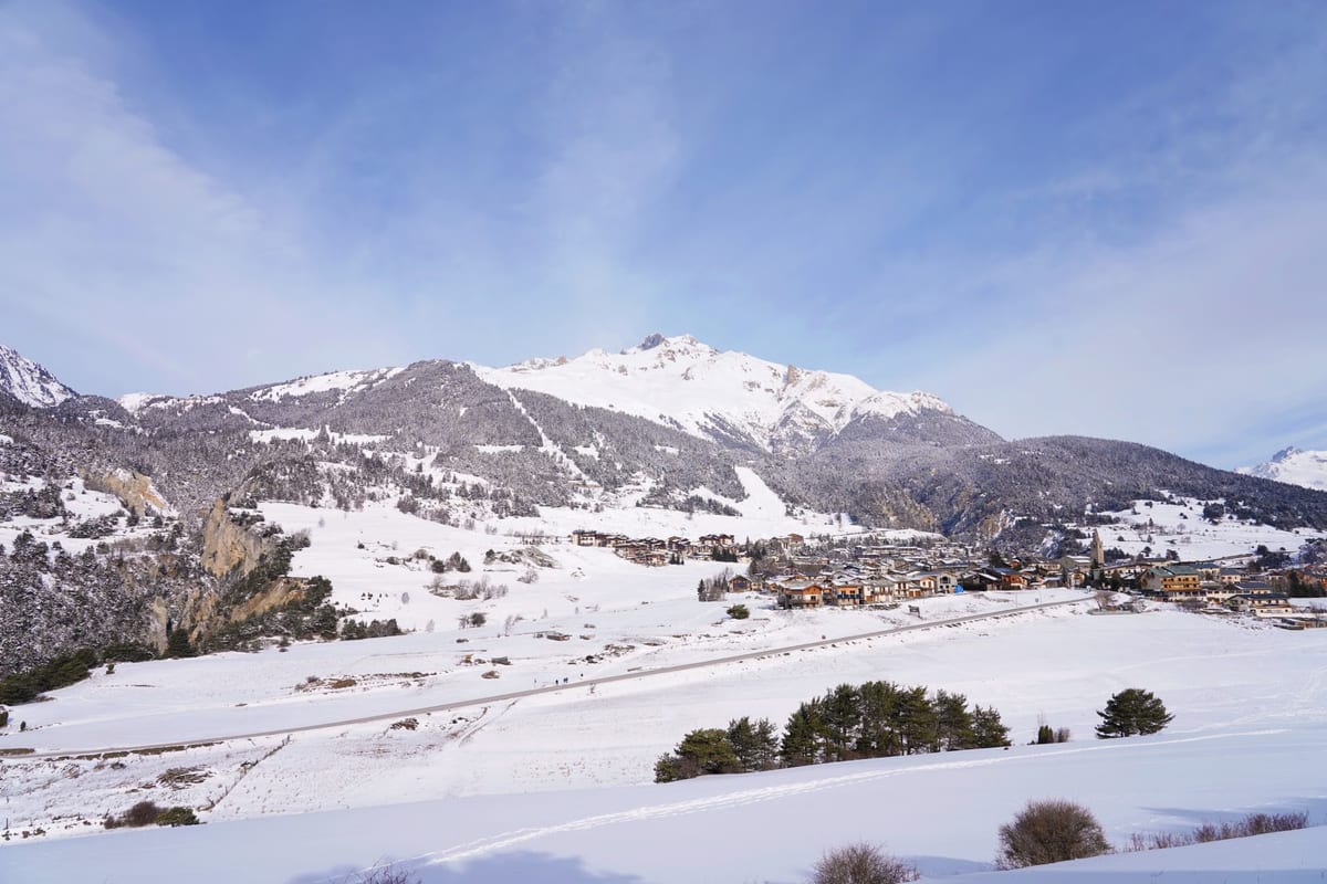Verschneites Alpental mit einem Bergdorf und schneebedeckten Gipfeln unter blauem Himmel