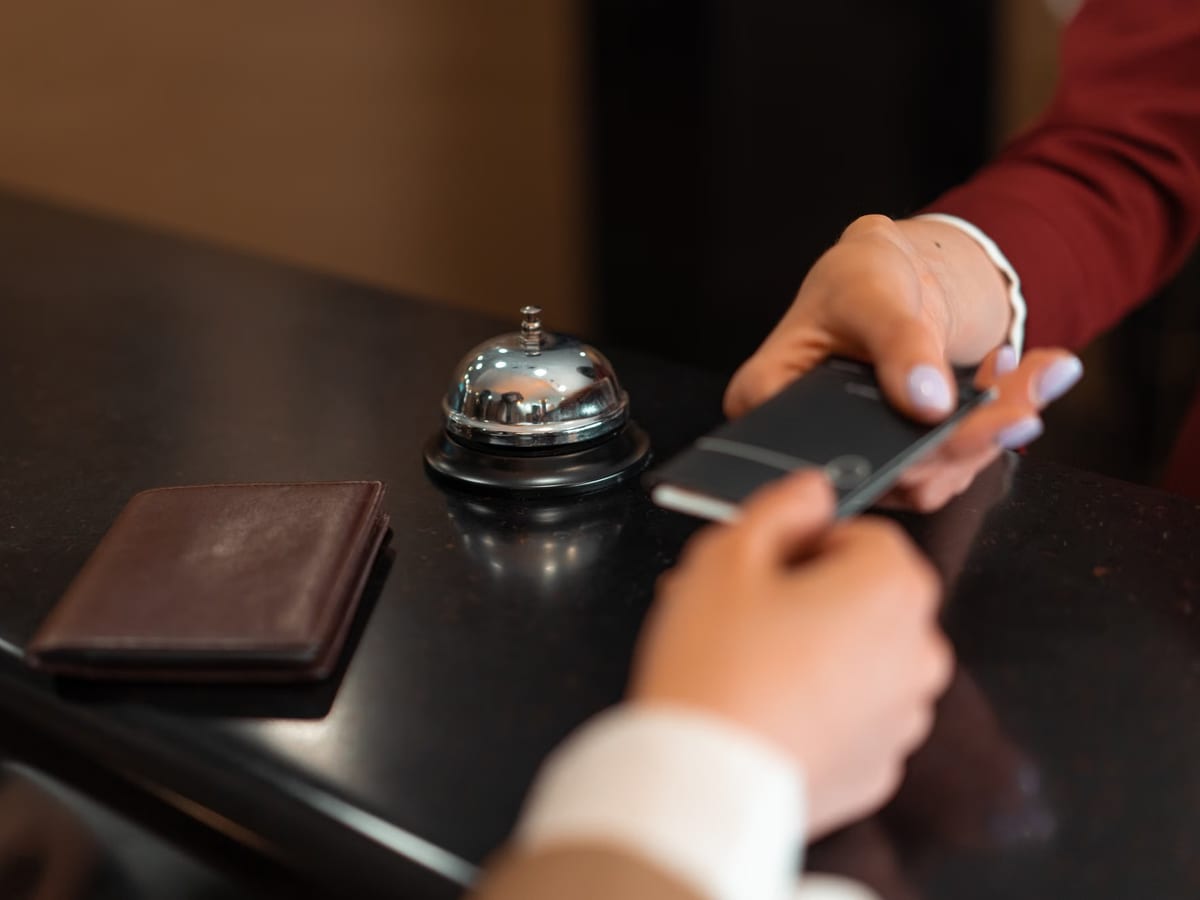 Übergabe eines Smartphones über einen Empfangstresen mit Rezeptionsklingel und Brieftasche
